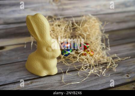 Un coniglietto pasquale al cioccolato bianco sulla cima di un mucchio di fieno con uova di cioccolato sullo sfondo Foto Stock
