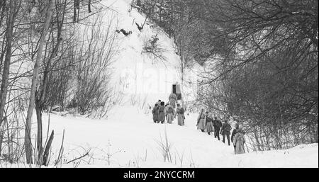 Gli uomini vestiti come soldati della Guardia Bianca dell'esercito imperiale russo nella marcia della Guerra civile Russa attraverso la foresta invernale innevata. Rievocazione storica Foto Stock