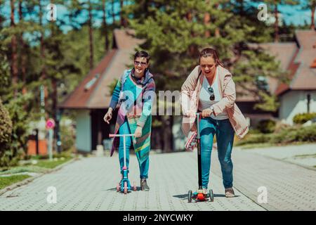 Due donne che si divertono nel parco mentre cavalcano uno scooter Foto Stock