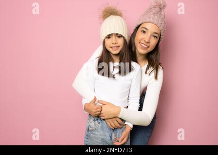 Divertente sorridente giovane donna e bambina sorelle ragazza vestendo casual t-shirt hugging guardando macchina fotografica isolato su colore rosa sfondo studio ritratto Foto Stock