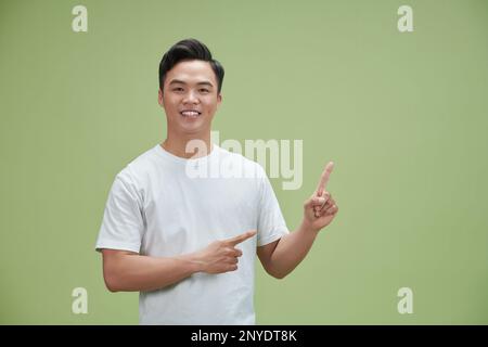 Ritratto di giovane sorridente bell'uomo asiatico che punta le dita in uno spazio vuoto a parte Foto Stock