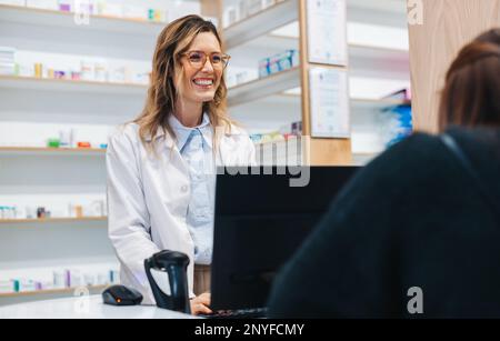 Farmacista femminile che assiste un paziente al banco in una farmacia. Un operatore sanitario amichevole che dispensa farmaci in farmacia. Foto Stock