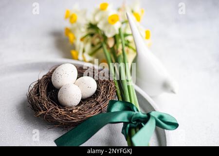 Dall'alto tavolo della cena di pasqua con uova nel nido e fiori di daffodil su sfondo di cemento Foto Stock