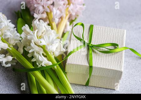 Da sopra piatto di giacinto fiori vicino scatola regalo con nastro su sfondo di cemento Foto Stock