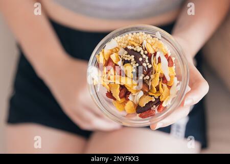 Dall'alto femmina tagliata irriconoscibile mangiare muesli sani e noci Foto Stock