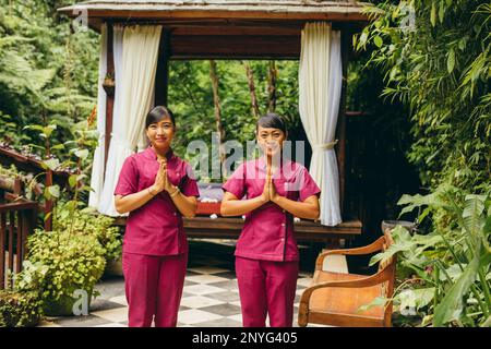 Foto all'aperto di due massaggiatrici che accolgono gli ospiti al centro benessere di bellezza, con le mani unite per salutare. Massaggiatrice professionale. Foto Stock