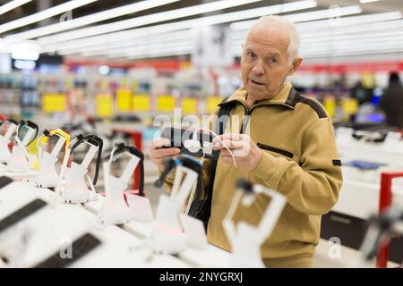 uomo anziano in grigio pensionato esaminano il contatore con gadget elettronici e tablet in showroom del negozio di merci digitali Foto Stock