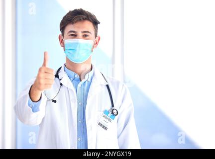 Ritratto, dottore e uomo con i pollici in su, maschera e successo per cura, diagnosi e conformità di sicurezza. Copertura facciale, maschio e medico con Foto Stock