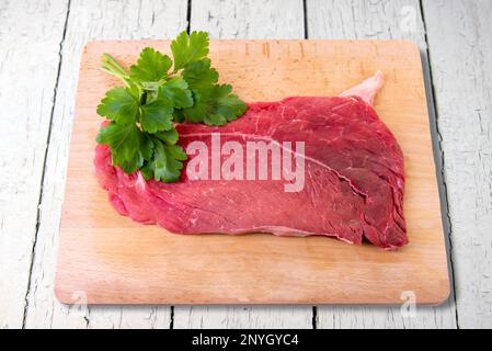 Bistecca di manzo crudo sul tagliere di legno con foglie di prezzemolo isolate sul percorso di taglio bianco Foto Stock