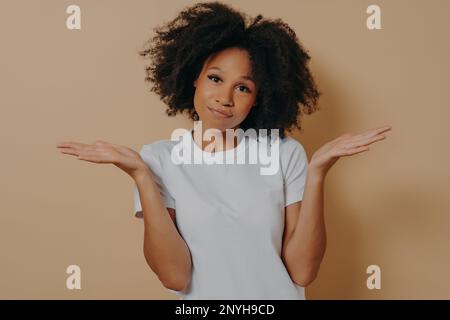 Giovane donna africana dubbiosa che alza le palme con esitazione e guarda la telecamera con espressione del volto perplesso, misto razza femmina essendo incerto e havi Foto Stock