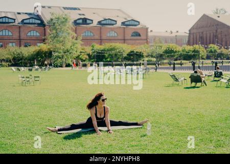 Foto di giovane attiva modello femminile si spezza su kareMat focalizzato in distanza vestita in abbigliamento sportivo rimane flessibile motivati per l'allenamento pose outdo Foto Stock