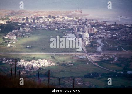 Vista panoramica verso est, del villaggio di confine di Sha Tau Kok, nuovi territori, Hong Kong, Cina 1984. Due giunchi a vela sono in riva al mare sul lato cinese del villaggio. In primo piano la linea di basi per un'estensione del confine HK/Cina Fence. Foto Stock