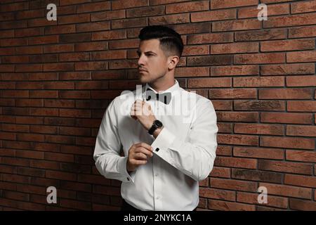 Bell'uomo elegante che si mette sul gemelli vicino al muro di mattoni Foto Stock