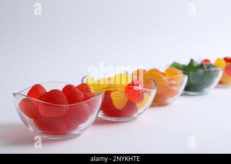 Diverse deliziose caramelle gommose in ciotole su fondo bianco Foto Stock