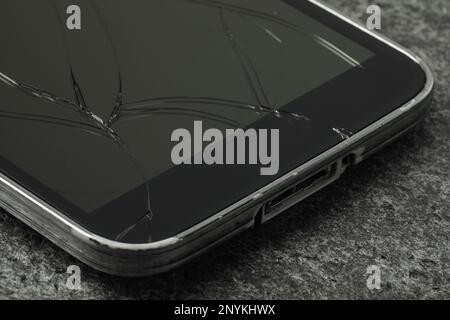 Smartphone con schermo incrinato su sfondo di pietra grigia, primo piano. Riparazione del dispositivo Foto Stock
