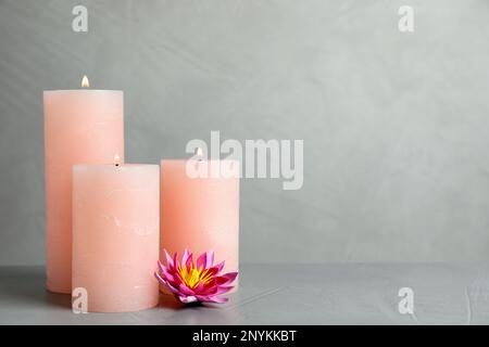 Candele brucianti e fiori di loto su un tavolo di pietra grigio chiaro. Spazio per il testo Foto Stock