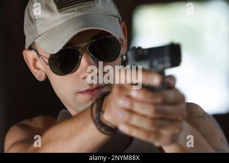 Ritratto di giovane soldato ucraino fresco in occhiali da sole che punta con una pistola a criminale Foto Stock