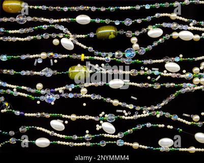 Alcuni lucido stringhe di tallone isolato su sfondo nero. Molti collana decorativa filettature nella forma di onde Foto Stock