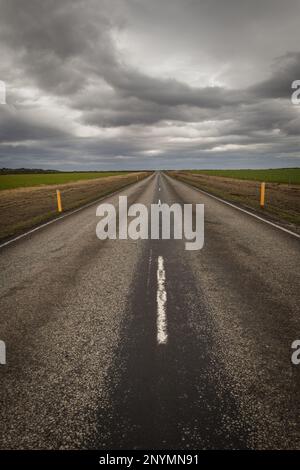 Una ripresa verticale di una strada che si estende attraverso un paesaggio di campi erbosi sotto un cielo nuvoloso Foto Stock