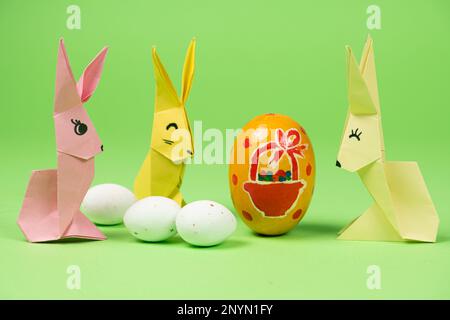 Origami di Pasqua - tre coniglietti di carta e uova, sfondo verde. Artigianato per le vacanze, fatelo da soli Foto Stock