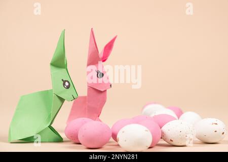 Due coniglietti di origami di carta e un uovo di Pasqua su sfondo beige. Artigianato con le proprie mani per Pasqua Foto Stock