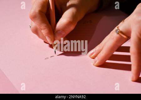 Vista ripresa ritagliata delle mani della donna che scrive qualcosa in una lettera rosa. Foto Stock