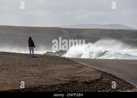 Lady guardando forti onde che si schiantano sulle rocce da lontano. Ajuy, Fuerteventura. Foto Stock