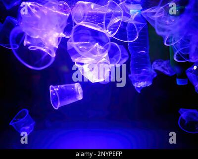 Tazze e bottiglie di plastica rifiuti che sgocciolano in un illuminato blu luci acqua, monocromatico, inquinamento ambientale globale, rifiuti subacquei Foto Stock