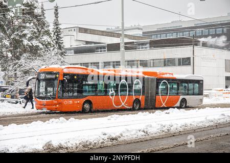 Autobus elettrico articolato sulla linea 20 alla fermata di Haartmaninkatu in una grigia giornata invernale nel quartiere Meilahti di Helsinki, Finlandia Foto Stock