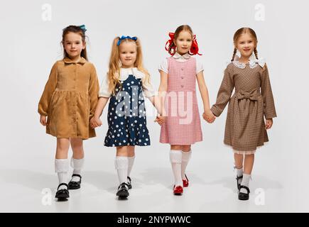 Quattro belle bambine, bambini in abiti retrò di tendenza in posa, a piedi contro sfondo grigio studio. Concetto di infanzia Foto Stock