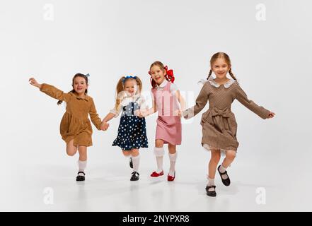 Quattro belle bambine, i bambini in abiti retrò di stile posa, che corrono sullo sfondo grigio studio. Concetto di infanzia Foto Stock