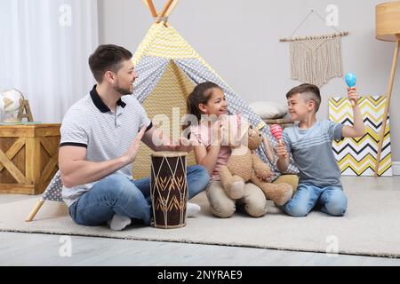 Il padre e i bambini giocano vicino al giocattolo wigwam a casa Foto Stock