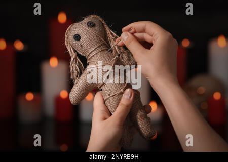 Donna che pugnalcia bambola voodoo con spilla in stanza scura, primo piano. Maledizione cerimonia Foto Stock