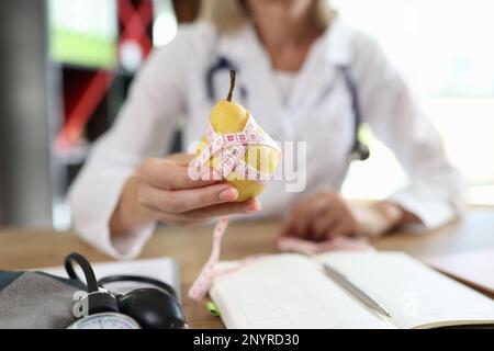 Medico nutrizionista che tiene la pera gialla matura con il nastro di misurazione Foto Stock