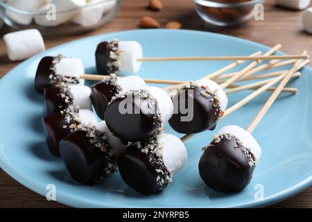 Deliziosi marshmallows ricoperti di cioccolato e noci schiacciate su piatto, primo piano Foto Stock