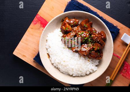 Concetto di cibo Asiatico dolce smaltato maiale e riso su sfondo di pietra ardesia nera con spazio copia Foto Stock