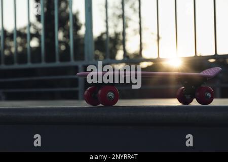 Moderno skateboard rosa con ruote rosse sulla rampa all'aperto al tramonto Foto Stock