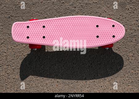 Moderno skateboard rosa con ruote rosse su strada asfaltata all'aperto, vista dall'alto Foto Stock