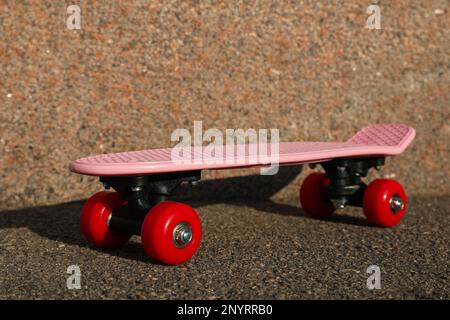 Skateboard rosa con ruote rosse su asfalto all'aperto Foto Stock