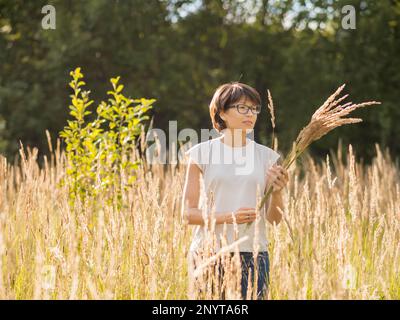 La donna sta raccogliendo erba secca sul campo autunnale. Fiorista al lavoro. Usando le piante essiccate come bouquet decorativo per l'interno domestico. Foto Stock