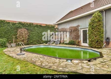 un cortile con una piscina al centro e piante verdi che crescono dall'altro lato della casa dietro di esso Foto Stock