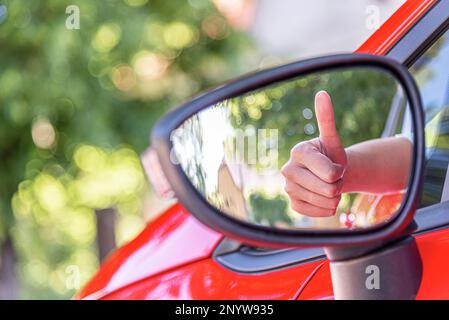 Il pollice in su della mano di una donna è riflesso nello specchio dell'automobile. Foto Stock