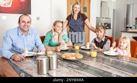 Vita familiare, tavolo per la colazione. Una giovane madre che serve la colazione di famiglia. Da una serie di immagini correlate. Foto Stock