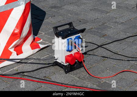 Distributore di elettricità portatile su una strada asfaltata. I fili elettrici neri e rossi si trovano a terra. Foto Stock