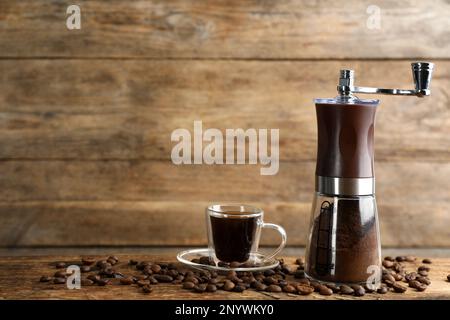 Macinacaffè manuale con polvere, fagioli e tazza di bevanda su tavola di legno. Spazio per il testo Foto Stock