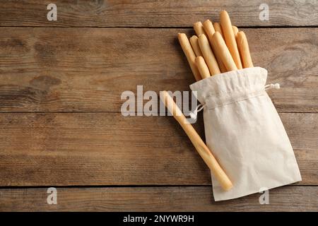 Deliziosi grissini bastoncini in sacchetto su tavolo di legno, piatto. Spazio per il testo Foto Stock