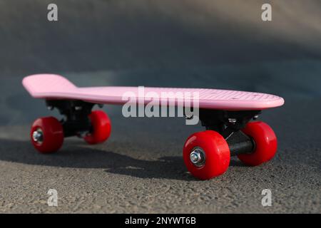 Moderno skateboard rosa con ruote rosse su strada asfaltata all'aperto Foto Stock