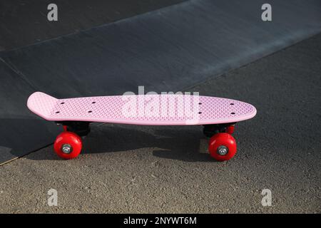Moderno skateboard rosa con ruote rosse su strada asfaltata all'aperto Foto Stock
