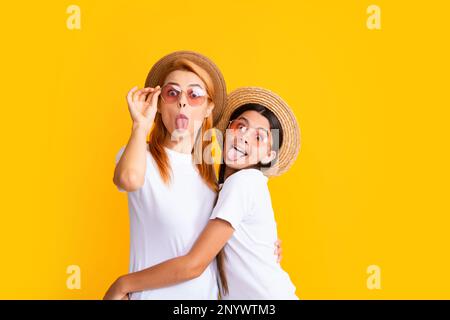 Studio ritratto di divertente bambino con mamma mostra lingua. Faccia divertente. Mamma e figlia adolescente che abbraccia una bella coccole, indossando t-shirt bianche cappello di paglia e. Foto Stock