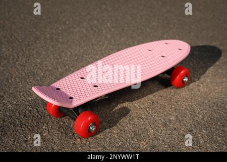 Skateboard rosa con ruote rosse su asfalto all'aperto Foto Stock